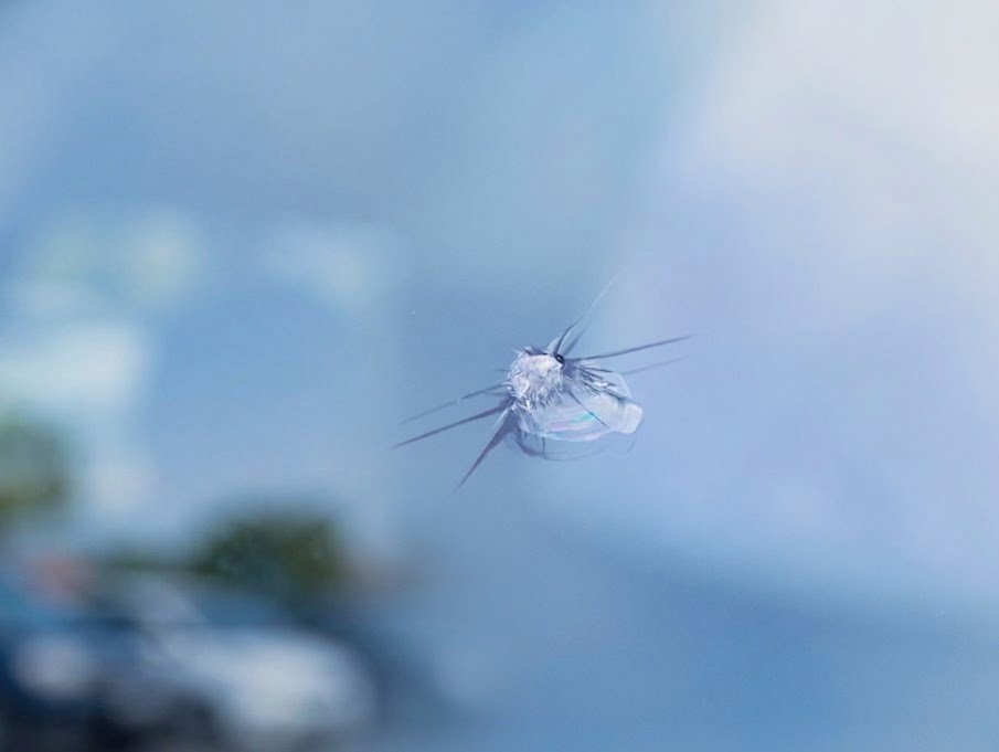Star-break rock chip in a windshield, with blurred sky and traffic visible through the glass